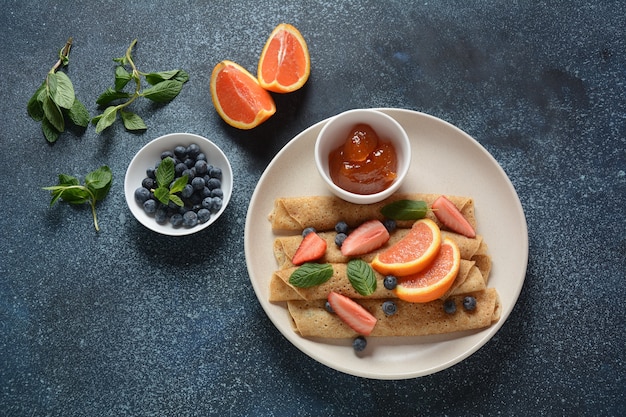 Sweet pancakes wrapped with fresh mint strawberries blueberries oranges and jam