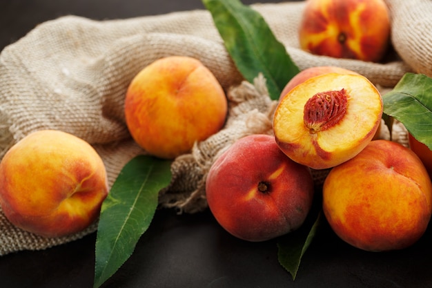 Sweet Peaches on a sharp stone table with a cloth of burlap and a slice of juicy peach with a bone.