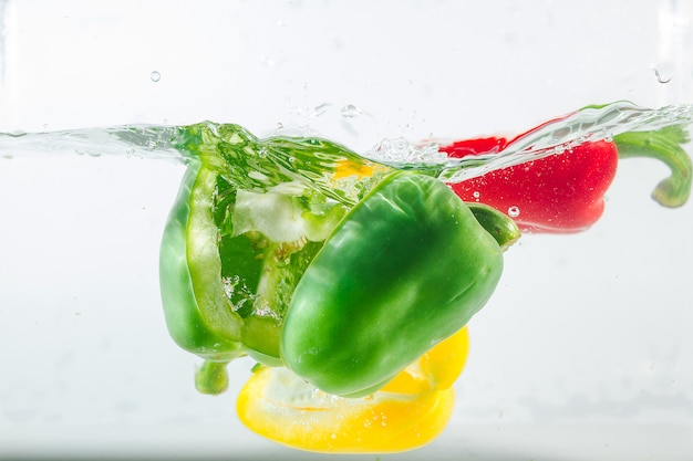 Foto il peperone dolce nel giallo, rosso, verde spruzza dell'acqua, peperone dolce su bianco