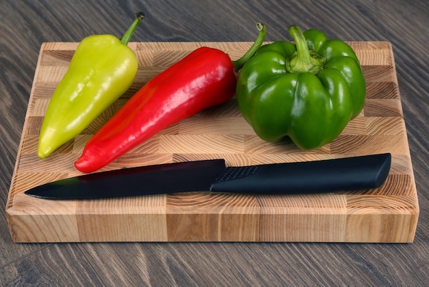 Sweet peppers with a ceramic knife on a wooden board