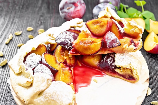 Photo sweet pie with plum, sugar and cardamom on paper, sprigs of green mint on wooden board background