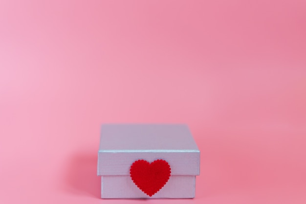 Photo sweet pink background with a silver gift box and decoration seal with a craft little red heart symbol of love and care