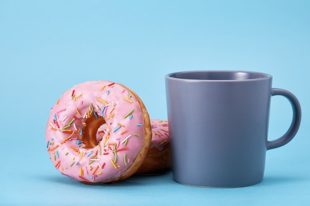 Sweet pink donuts with a blue mug on a blue background. Concept dessert, sweet life, we are what we eat. Blue background, copy space.