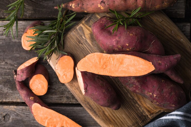 Sweet potato on wooden board background, close up. Raw sweet potatoes or batatas with herbs