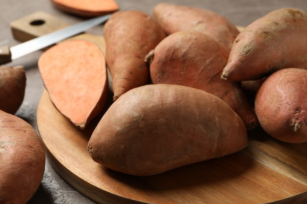 Sweet potatoes, board and knife on grey surface