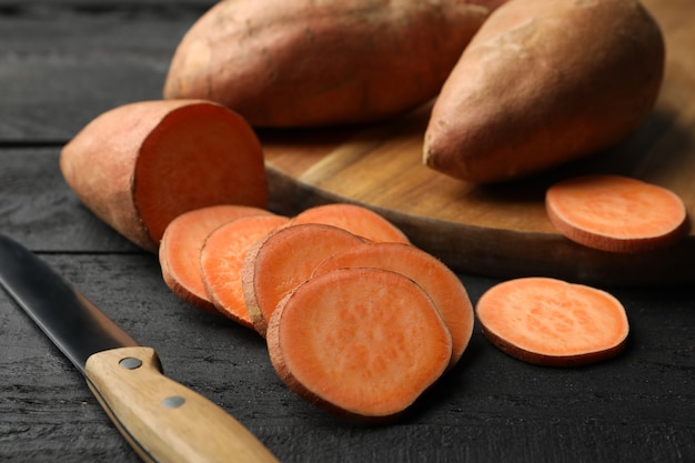 Sweet potatoes, board and knife on wooden surface