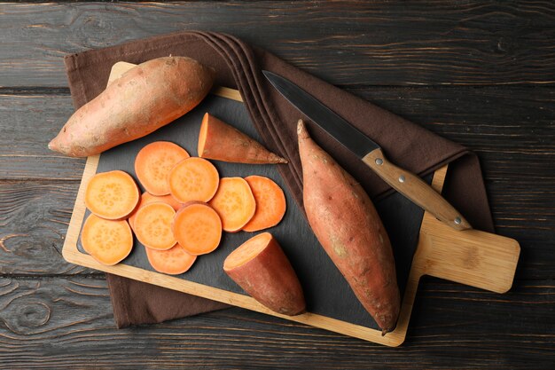 Sweet potatoes, board and towel on wooden surface