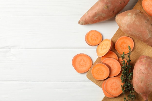 Sweet potatoes and board on white wooden surface