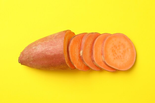 Sweet potatoes and slices on yellow surface