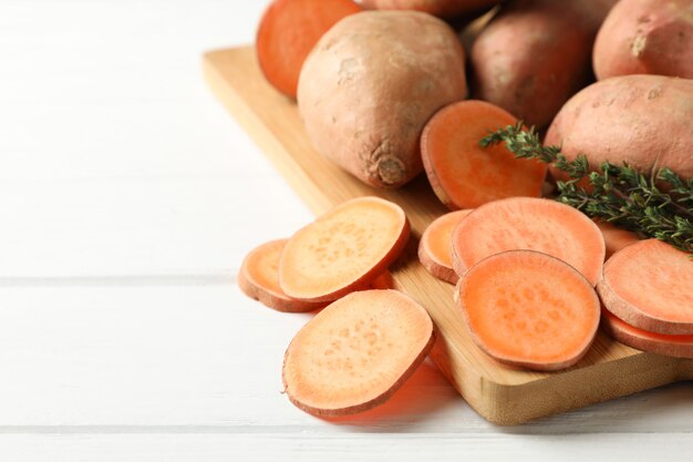 Sweet potatoes, thyme and board on white wooden surface