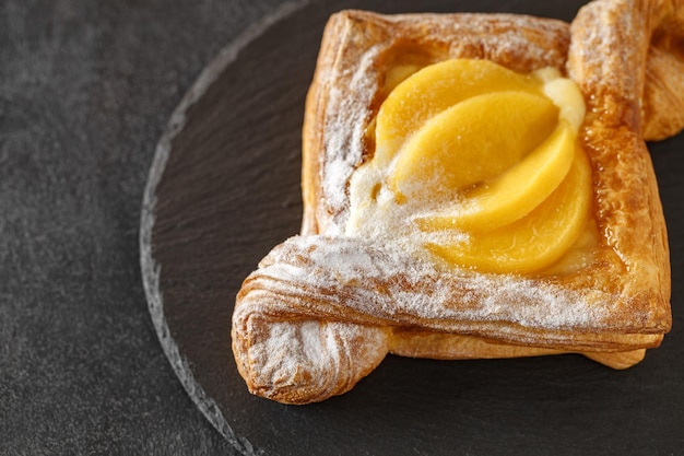 Sweet puff pastry with peaches cream and powdered sugar on slate stone plate round dark background selective focusxA