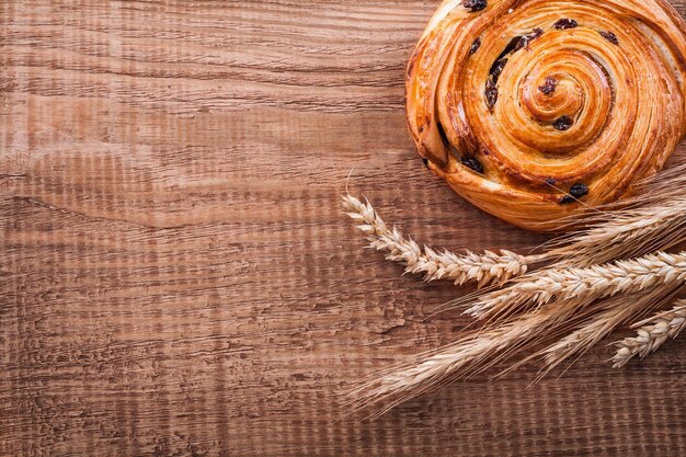 Sweet raisin bun bunch of wheat ears on oak wooden board food and drink concept