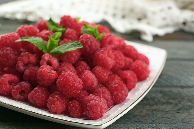 Sweet raspberries on plate on wooden background