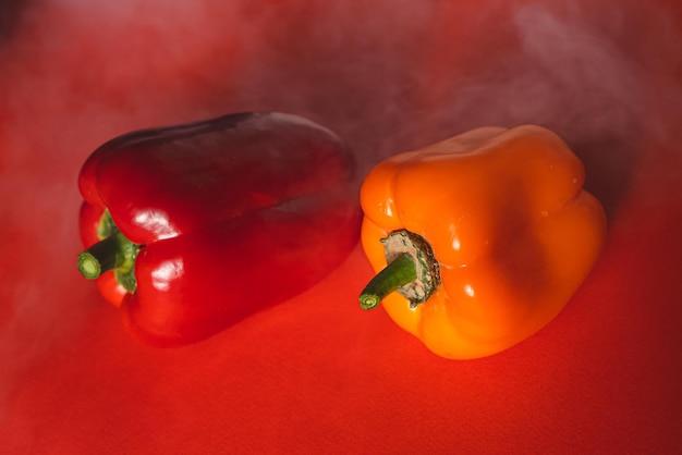 Photo sweet red and orange peppers on a red background with a light smoke