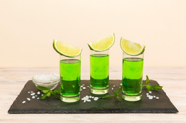 Sweet refreshing mint liqueur with ice and mint leaves on table background Shots with lime slice and mint flat lay