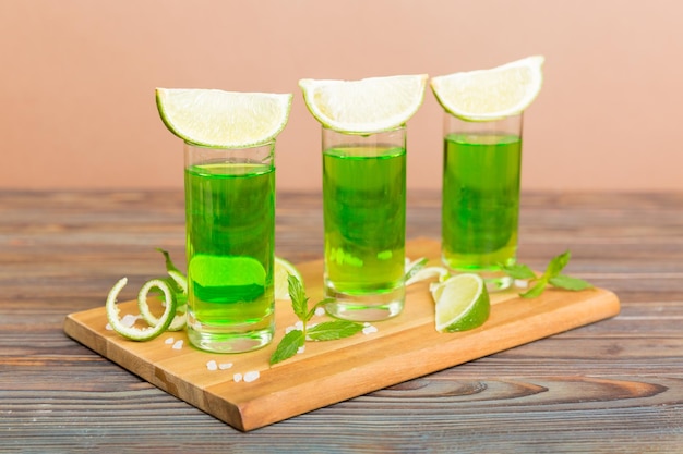 Sweet refreshing mint liqueur with ice and mint leaves on table background Shots with lime slice and mint flat lay