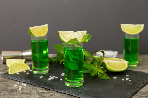 Sweet refreshing mint liqueur with ice and mint leaves on table background Shots with lime slice and mint flat lay