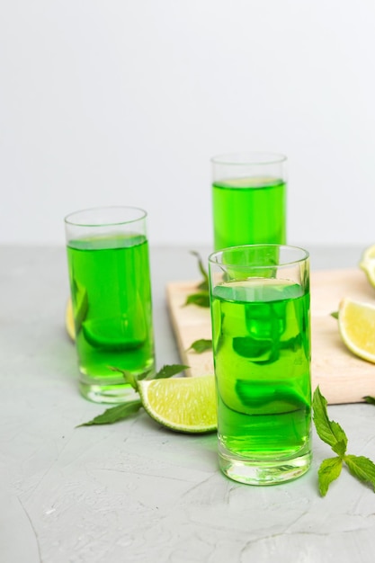 Sweet refreshing mint liqueur with ice and mint leaves on table background Shots with lime slice and mint flat lay