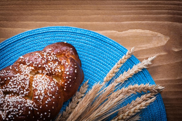 Sweet roll wheat rye ears with blue wattled cover on wooden board food and drink concept