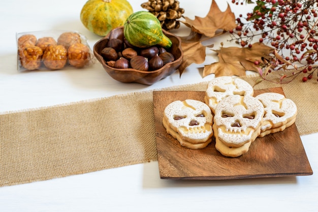 Photo sweet skull biscuit on the wooden plate, chestnuts and pumpkins on the table, prepared for halloween.