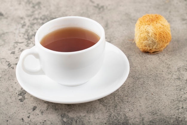 Sweet snacks with white cup of tea placed on a stone table .