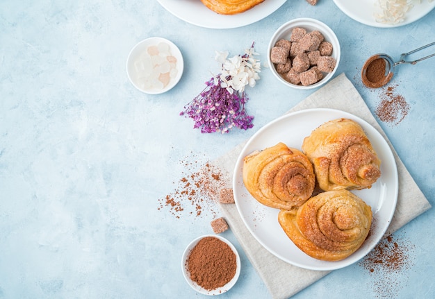 Sweet snail buns with cocoa and sugar and flowers on a light blue background.