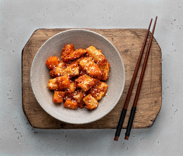 Photo sweet and sour chicken in a ceramic bowl on a light background, top view