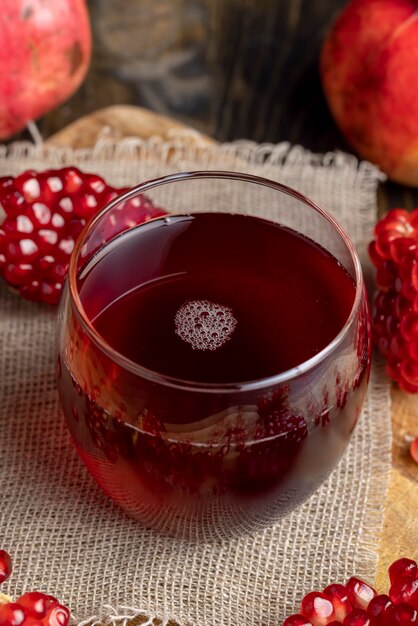 Sweet and sour pomegranate juice in a transparent glass on the table next to it are red ripe pomegranates with large sweet grains