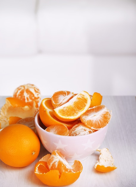 Sweet tangerines and oranges on table in bowl in room