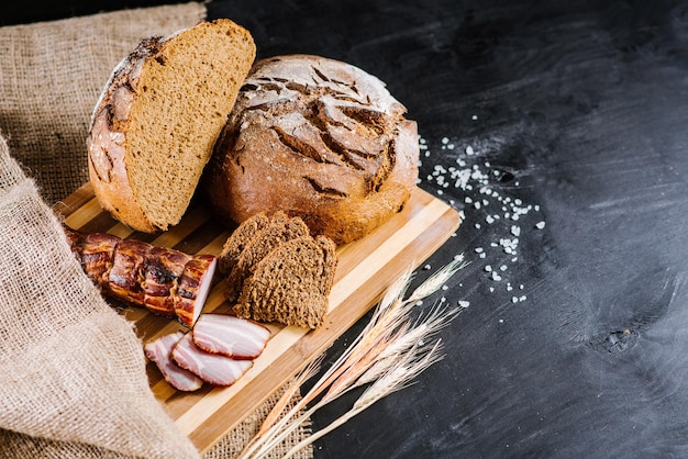 Sweet and tasty bread and wheat on black wooden background