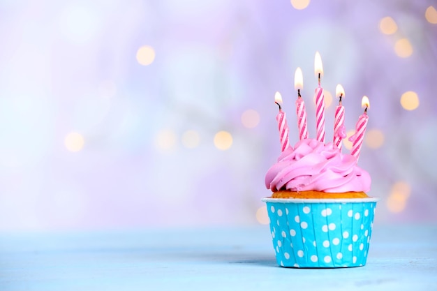 sweet tasty cupcake with candles on blue wooden table against blurred background