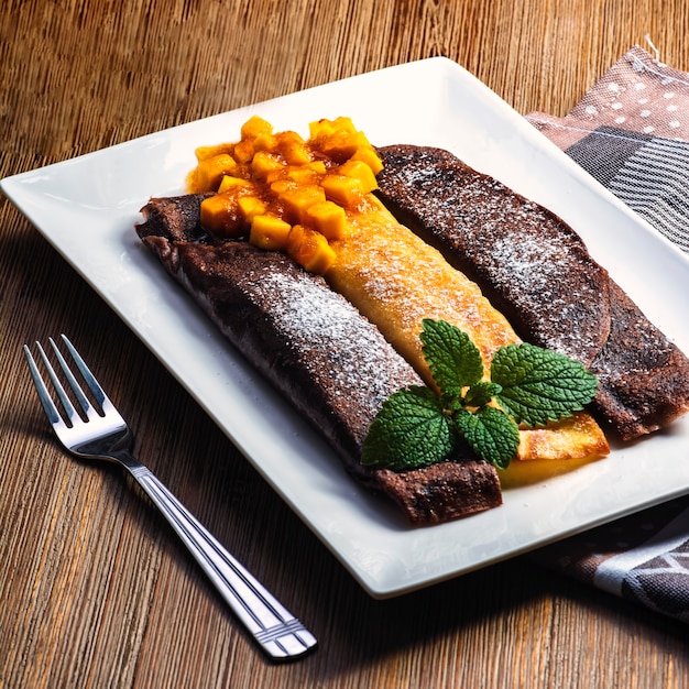 Фото Сладкий вкусный блинчик, домашний блинчик с шоколадом. здоровая и вкусная еда с ежевикой, фруктами манго и мятой.