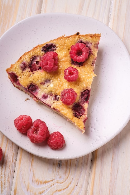 Sweet tasty pie slice with jellied and fresh raspberry fruits in plate, wooden table table, angle view