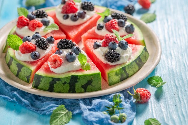 Foto dolce e gustosa pizza di cocomero con bacche, panna montata e foglie di menta, frutta coltivata in casa