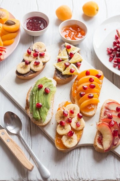 sweet toast with jam and various fruits apricots, peaches, bananas, oranges and avocado decorated with pomegranates on top.