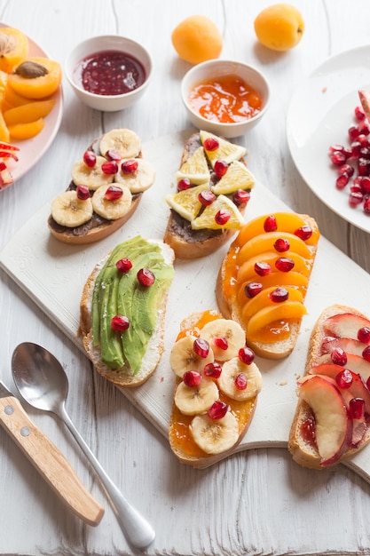 Toast dolce con marmellata e albicocche di vari frutti, pesche, banane, arance e avocado decorato con melograni in cima.