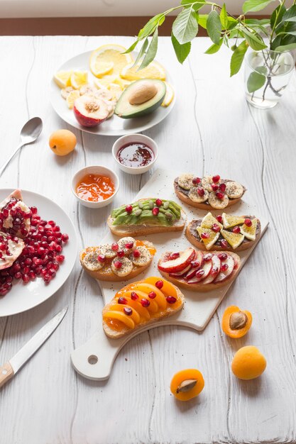 Foto toast dolce con marmellata e albicocche di vari frutti, pesche, banane, arance e avocado decorato con melograni in cima.