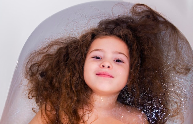 Photo sweet toddler baby girl in bath. child girl bathes in a white bathtub.