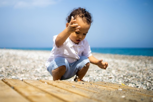 Ragazzo dolce del bambino che gioca con il ciottolo sulla spiaggia vicino al mare