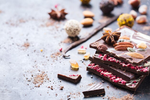 Sweet and treat junk unhealthy food Assortment of chocolate bar and praline truffle with spices and nuts on black moody grunge table Copy space background