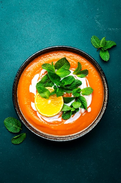 Sweet vegan pumpkin soup with coconut cream orange and mint Winter or autumn healthy vegetarian comfort food Soup bowl on green table background Top view