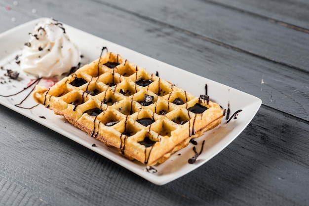 Сладкий вафельный десерт с шоколадом и мороженым на деревянном фоне