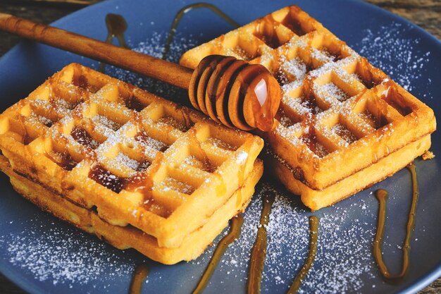 Sweet waffles drizzled with honey and sprinkled with powdered sugar on a blue plate