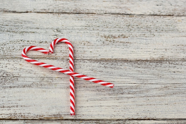 Sweet white and red candy canes in shape of heart on old wooden background. christmas holiday or valentine day concept