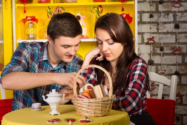 Sweet Young Lovers in Checkered Shirts Dating at the Shop with Pastry Basket and Drinks on the Table.