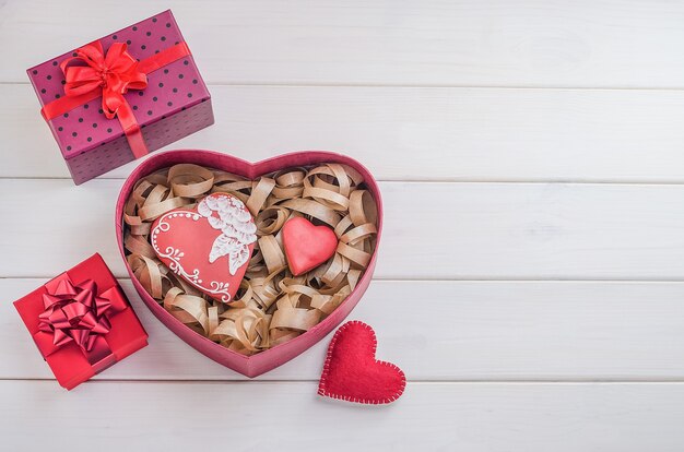 Sweets as a gift for Valentine's Day. Gingerbreads in the form of hearts with gifts with red ribbons with copy space on a white wooden background. Cooking, baking .-