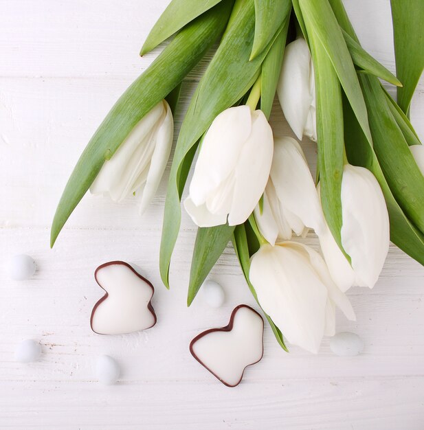 Foto dolci per festeggiare la pasqua. tulipani bianchi, uova di cioccolato e coniglietto di pasqua.