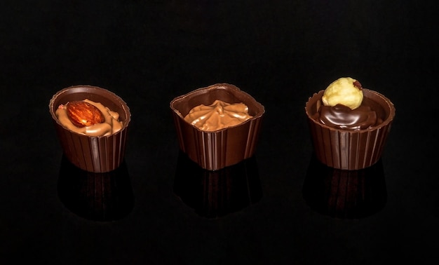 Sweets with cream and nuts on a black table. Assorted chocolate on black isolated background