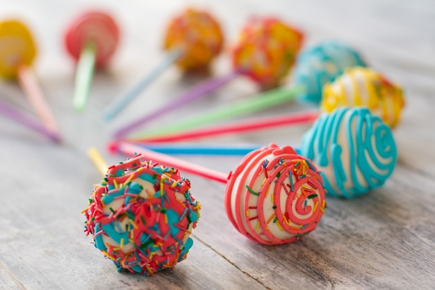 Sweets with frosting. Colorful candies on wooden surface. Cake pops for kids. Taste of a fun party.