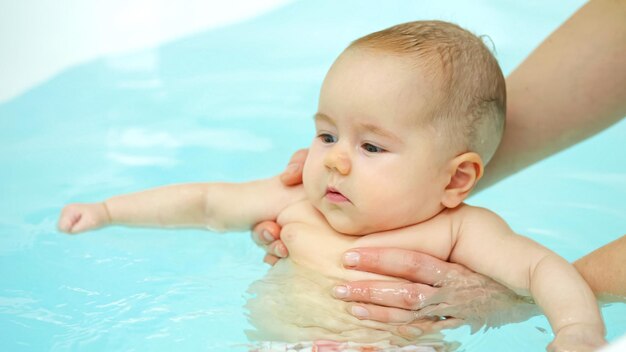 Swim teacher holds baby under arms girl swings legs in bathtub